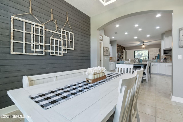 tiled dining area featuring wooden walls and ceiling fan