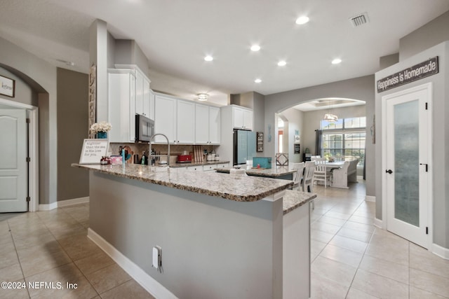 kitchen featuring fridge, backsplash, light tile patterned flooring, white cabinets, and light stone counters