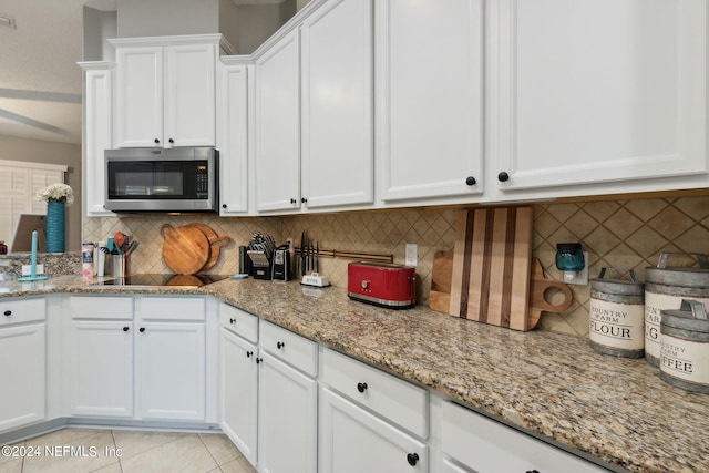 kitchen with light stone countertops, backsplash, black electric cooktop, white cabinets, and light tile patterned floors