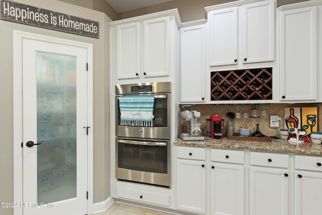 kitchen featuring light tile patterned flooring, backsplash, stainless steel double oven, white cabinets, and light stone counters