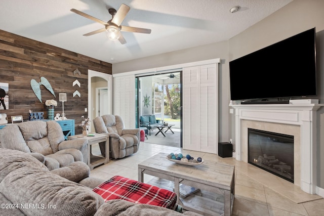 living room featuring a textured ceiling, wooden walls, light tile patterned floors, and ceiling fan