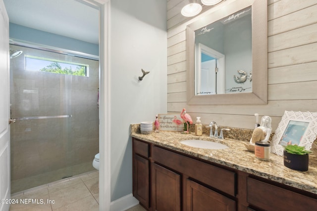 bathroom featuring a shower with door, tile patterned floors, toilet, vanity, and wood walls