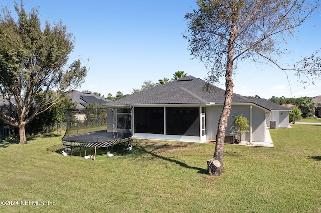 rear view of property with a sunroom, a lawn, and a trampoline