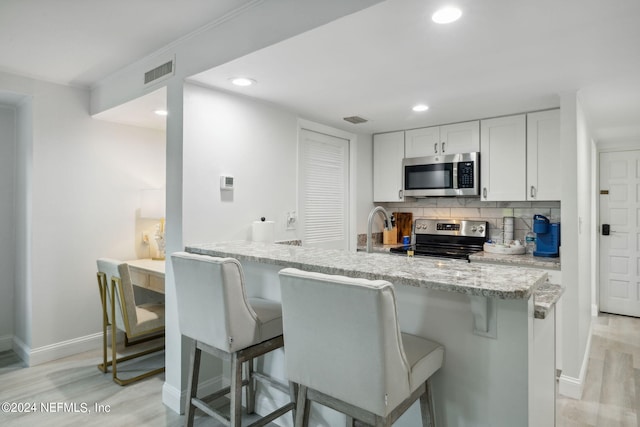 kitchen with a kitchen breakfast bar, appliances with stainless steel finishes, white cabinets, and light hardwood / wood-style floors