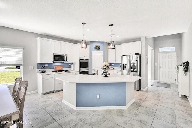 kitchen with pendant lighting, white cabinetry, stainless steel appliances, sink, and a center island with sink