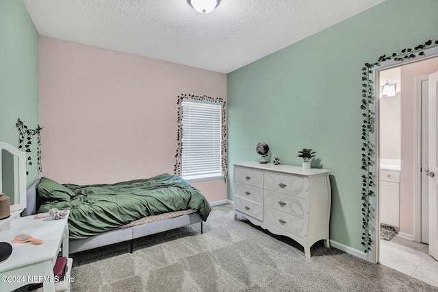 bedroom featuring a textured ceiling, ensuite bathroom, and light colored carpet