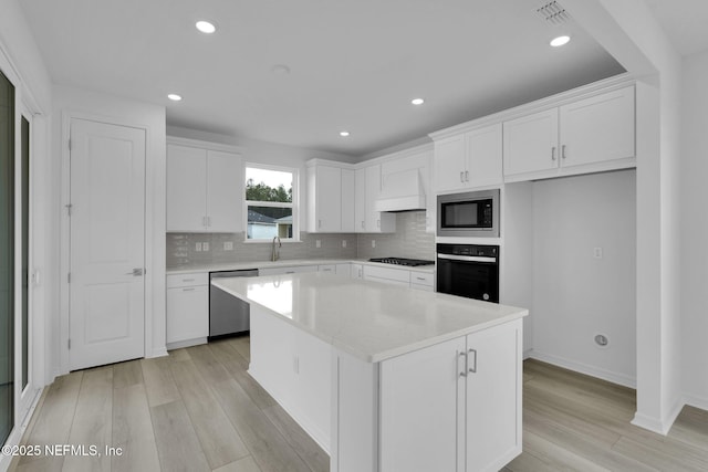 kitchen with white cabinets, custom range hood, a kitchen island, and black appliances