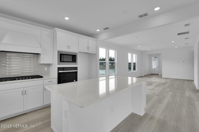 kitchen featuring a kitchen island, white cabinetry, decorative backsplash, black appliances, and light wood-type flooring