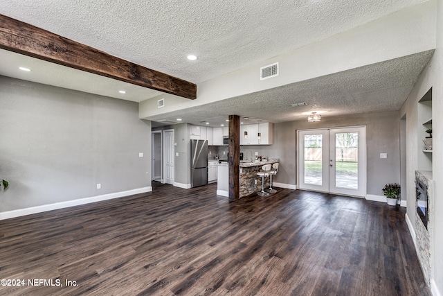 unfurnished living room featuring french doors, beamed ceiling, dark wood-type flooring, and a textured ceiling