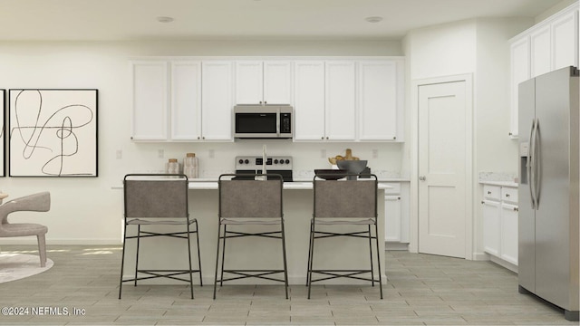 kitchen with stainless steel appliances, white cabinetry, a kitchen island with sink, and a breakfast bar area