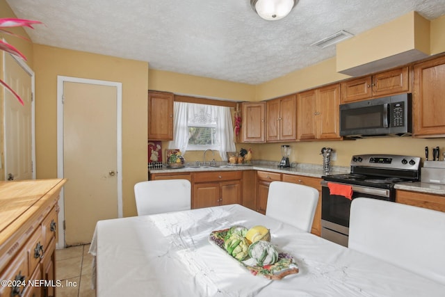 kitchen featuring sink, light tile patterned floors, stainless steel appliances, and a textured ceiling