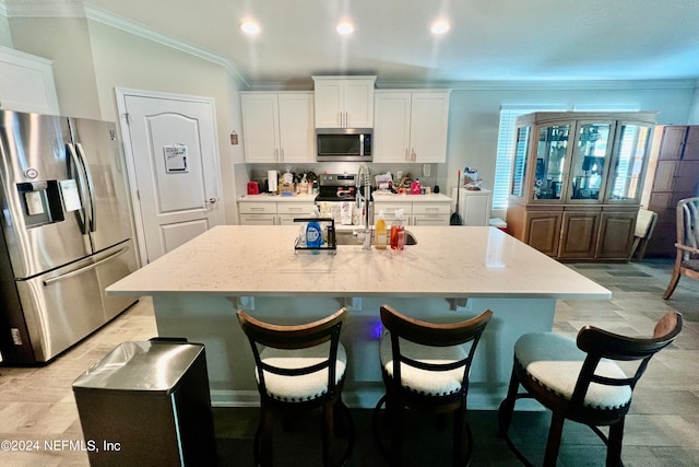 kitchen featuring white cabinets, stainless steel appliances, light stone countertops, and a kitchen island with sink