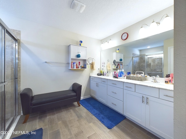 full bath with double vanity, visible vents, wood tiled floor, a sink, and a shower stall