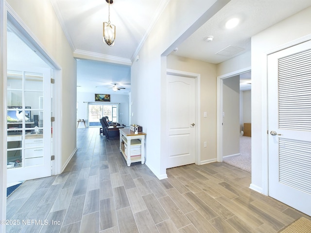 hallway with wood finish floors, visible vents, crown molding, and baseboards