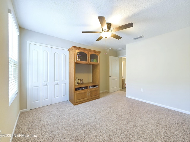 unfurnished bedroom featuring baseboards, visible vents, light colored carpet, a textured ceiling, and a closet