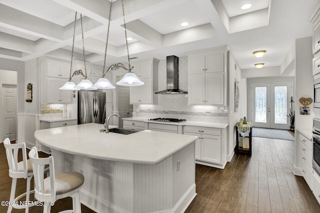 kitchen with wall chimney range hood, a spacious island, stainless steel appliances, and coffered ceiling