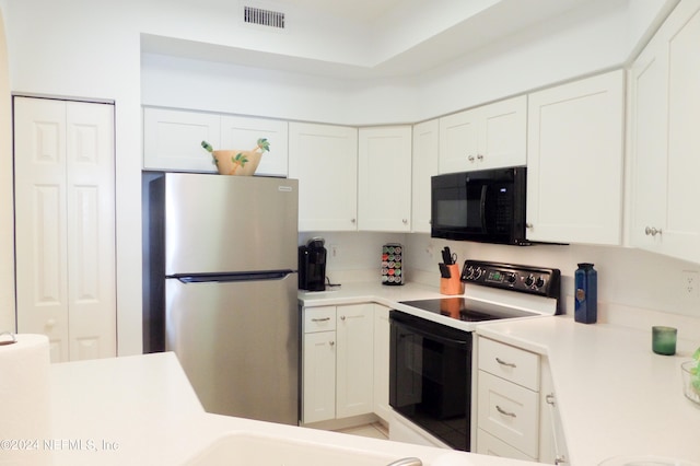 kitchen featuring visible vents, range with electric stovetop, white cabinetry, freestanding refrigerator, and black microwave