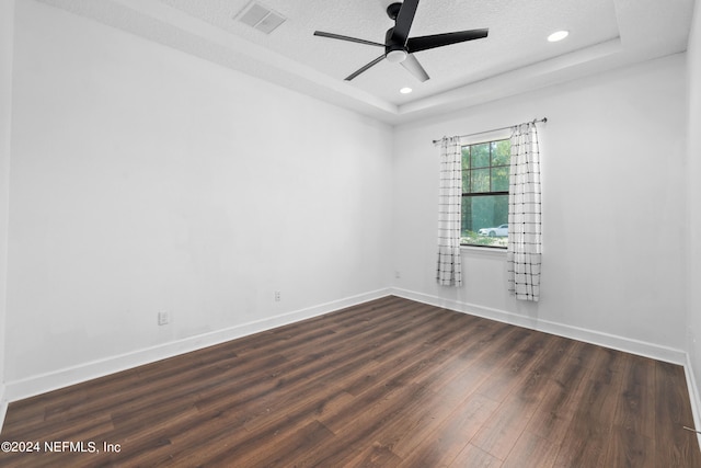 empty room featuring ceiling fan, dark hardwood / wood-style flooring, a textured ceiling, and a tray ceiling