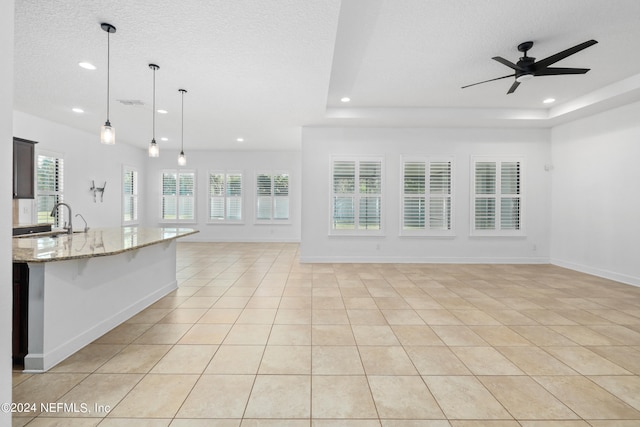 unfurnished living room featuring ceiling fan, sink, light tile patterned floors, and a textured ceiling