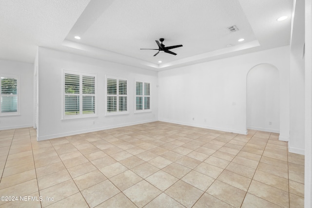 unfurnished room featuring ceiling fan, light tile patterned flooring, a textured ceiling, and a tray ceiling