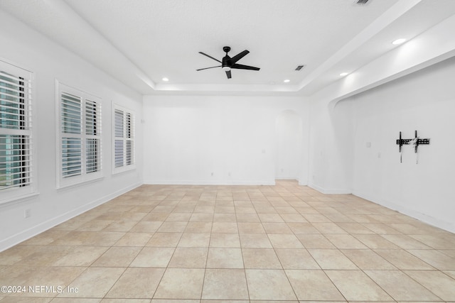 empty room featuring ceiling fan, a raised ceiling, and light tile patterned floors