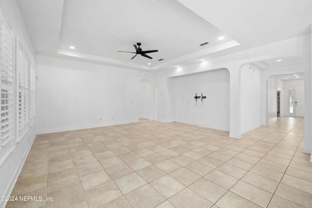 empty room featuring ceiling fan, light tile patterned flooring, and a tray ceiling