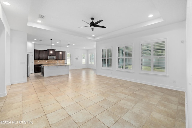 unfurnished living room with ceiling fan, a raised ceiling, and light tile patterned floors