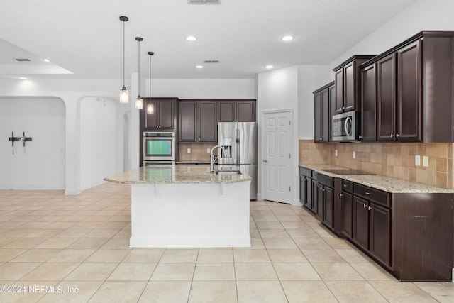 kitchen with light stone countertops, stainless steel appliances, tasteful backsplash, pendant lighting, and a center island with sink