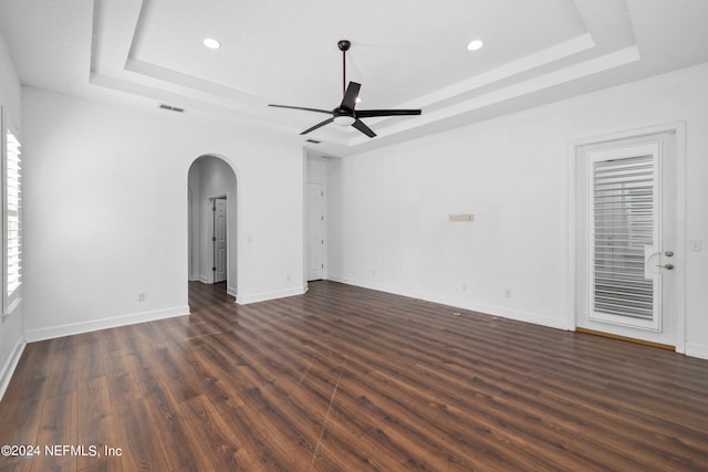 spare room with a raised ceiling, ceiling fan, and dark hardwood / wood-style flooring