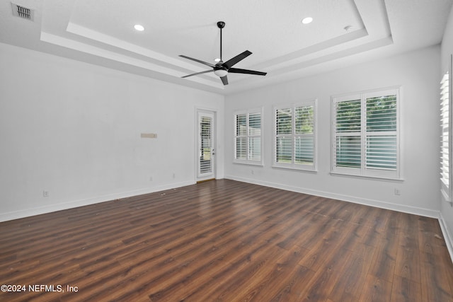 spare room with a textured ceiling, dark hardwood / wood-style flooring, a tray ceiling, and ceiling fan