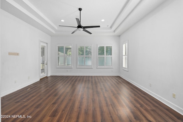 spare room with a tray ceiling, ceiling fan, and dark hardwood / wood-style flooring