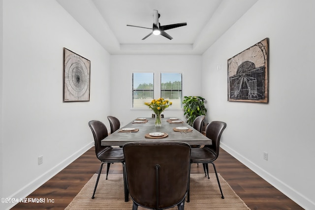 dining room with a raised ceiling, ceiling fan, and dark wood-type flooring