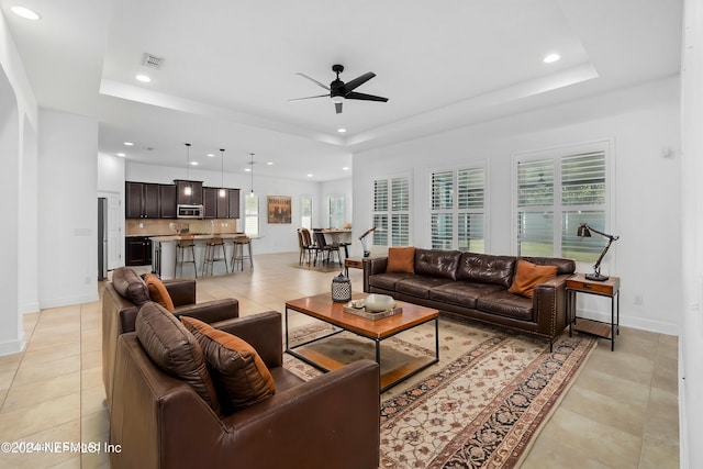 tiled living room featuring ceiling fan and a raised ceiling