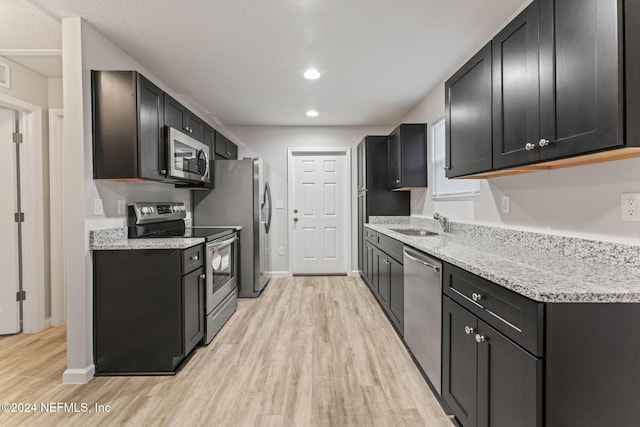 kitchen featuring sink, light stone countertops, appliances with stainless steel finishes, and light hardwood / wood-style flooring