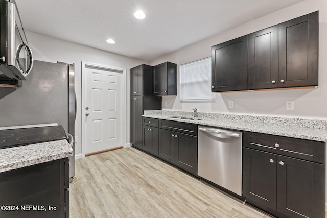 kitchen with sink, appliances with stainless steel finishes, light stone counters, and light wood-type flooring