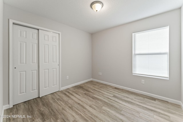 unfurnished bedroom featuring a textured ceiling, light wood-type flooring, and a closet