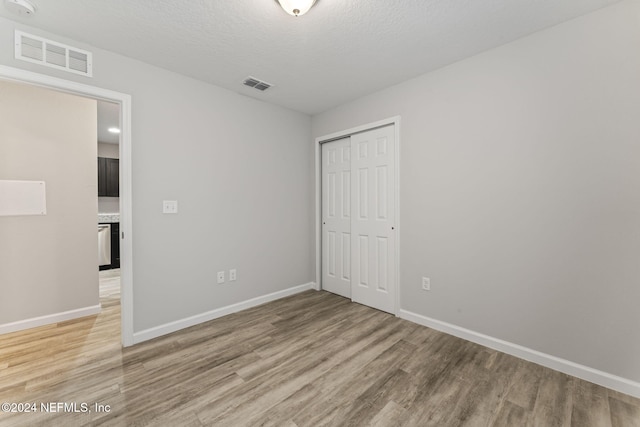 unfurnished bedroom featuring light hardwood / wood-style flooring, a textured ceiling, and a closet