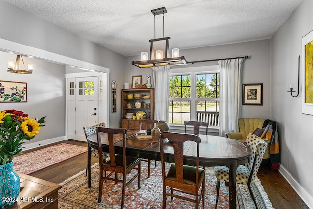 dining space with an inviting chandelier, a textured ceiling, and dark wood-type flooring