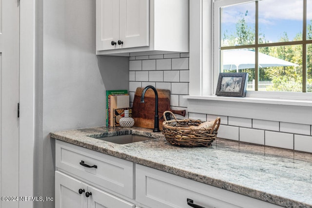 kitchen with white cabinetry, light stone counters, a healthy amount of sunlight, and decorative backsplash