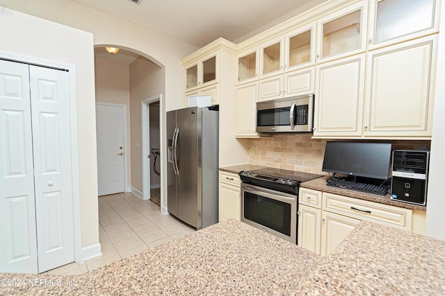 kitchen featuring decorative backsplash, cream cabinetry, stainless steel appliances, light tile patterned flooring, and light stone countertops