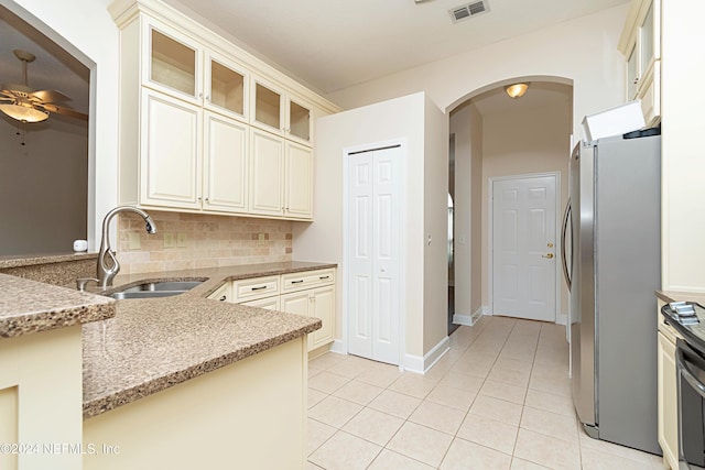 kitchen featuring sink, stainless steel fridge, light stone counters, decorative backsplash, and light tile patterned floors