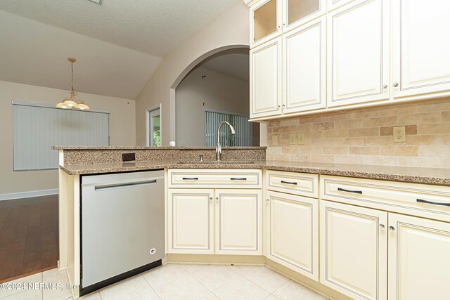 kitchen with lofted ceiling, backsplash, stainless steel dishwasher, cream cabinetry, and decorative light fixtures