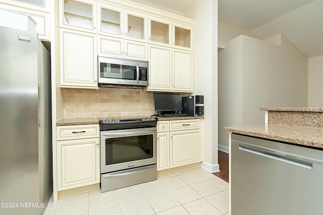 kitchen with light stone countertops, appliances with stainless steel finishes, backsplash, and light tile patterned floors