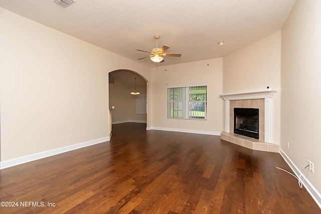 unfurnished living room featuring a tiled fireplace, a textured ceiling, dark hardwood / wood-style flooring, and ceiling fan