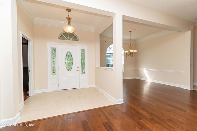 entryway with crown molding, a chandelier, and light wood-type flooring