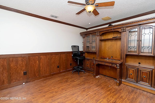 unfurnished office featuring hardwood / wood-style floors, built in desk, ceiling fan, a textured ceiling, and crown molding