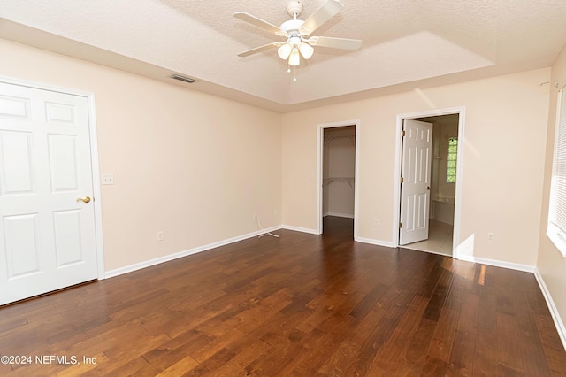 unfurnished bedroom with ceiling fan, a textured ceiling, a spacious closet, dark wood-type flooring, and ensuite bath