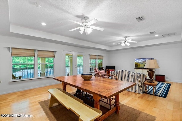 dining space featuring ceiling fan, a textured ceiling, a tray ceiling, light hardwood / wood-style floors, and french doors