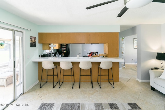 kitchen with kitchen peninsula, ceiling fan, a kitchen breakfast bar, light tile patterned floors, and stainless steel refrigerator