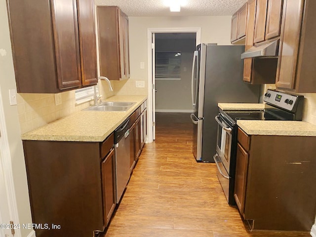 kitchen with backsplash, appliances with stainless steel finishes, a textured ceiling, light hardwood / wood-style flooring, and sink